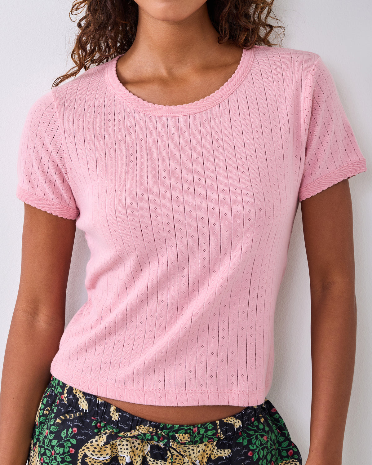 Pink short-sleeve pointelle top with scalloped neckline and sleeve edges, shown on a person.