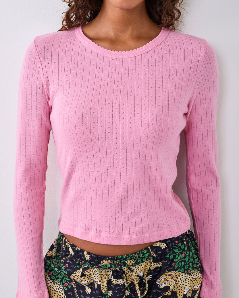 Pink long-sleeve pointelle top with a scalloped neckline, shown on a person with patterned pajama pants visible below.