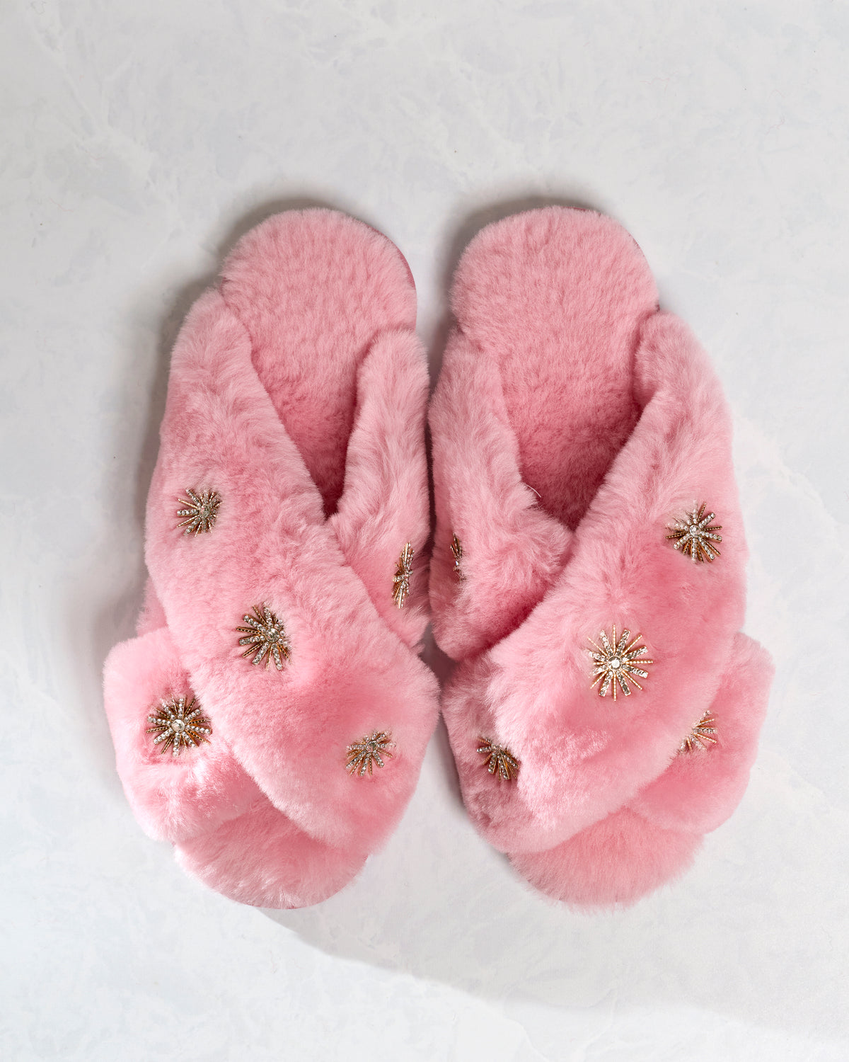 Pair of pink sheepskin slippers with rhinestone embellishments, shown from above.