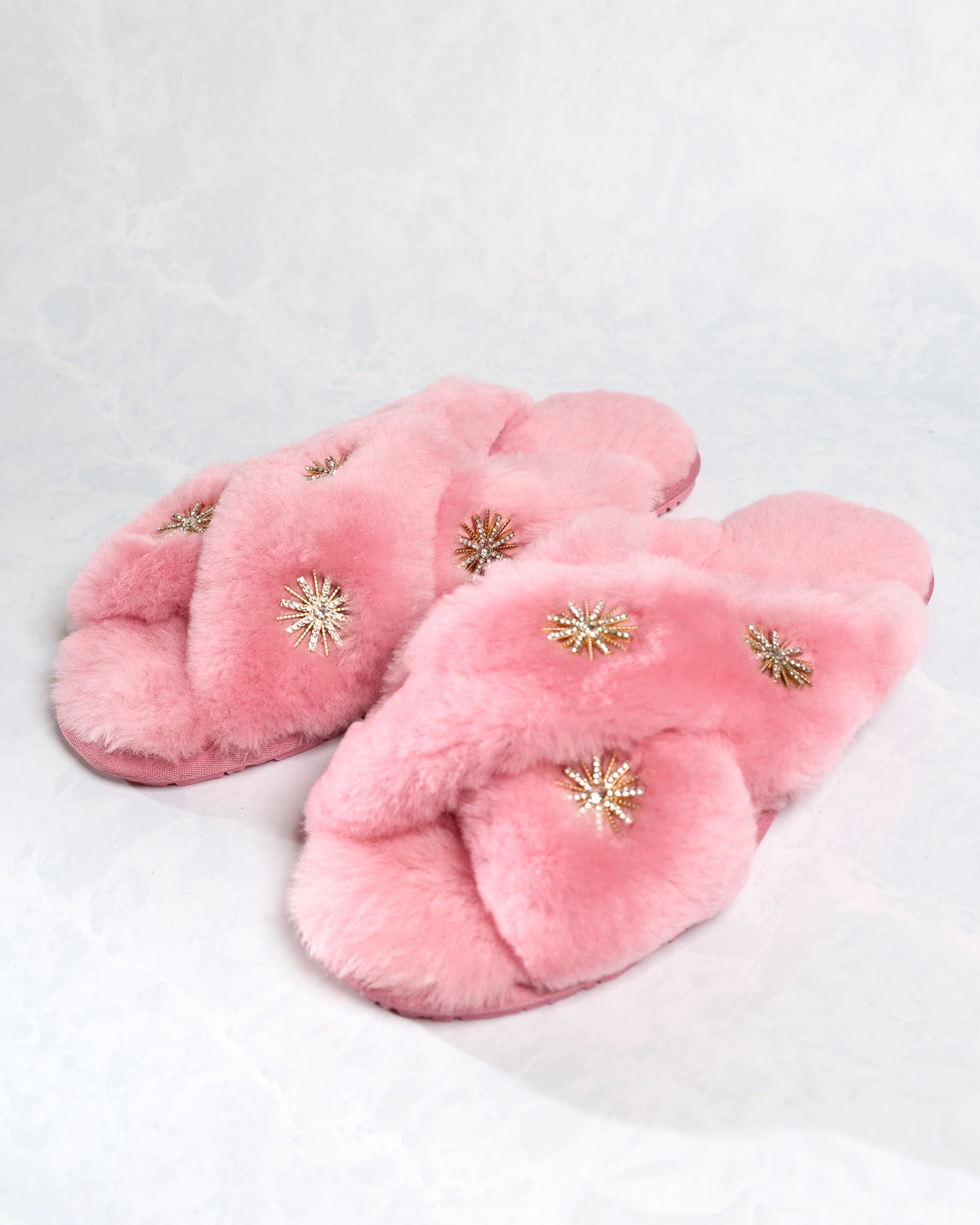 Pair of pink sheepskin slippers with rhinestone embellishments, shown at an angle.