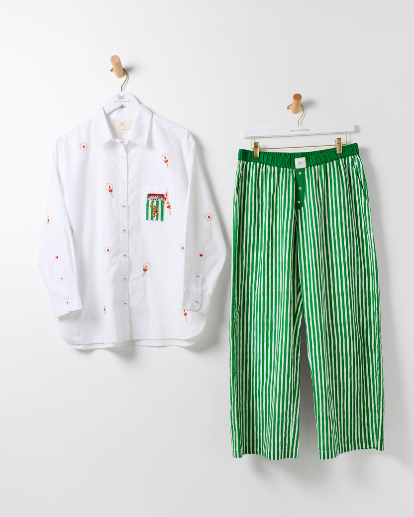 White embroidered button-down shirt and green-and-white striped pants hanging side by side.
