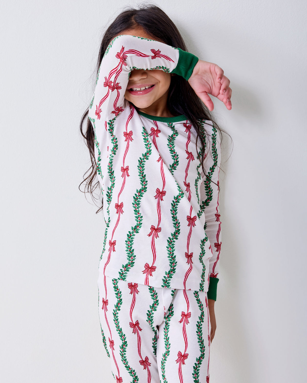 A child poses in white pajamas with vertical red ribbon and green garland prints.