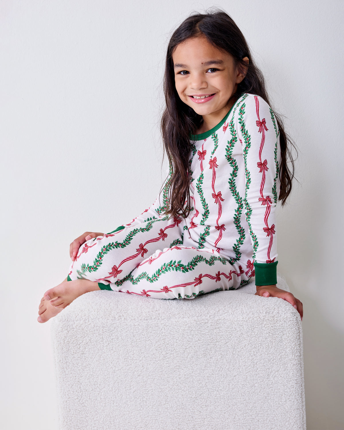 Child wearing the Ribbons & Bows Vanilla Cream kids long pajama set while seated, showing the pullover top and matching pants.