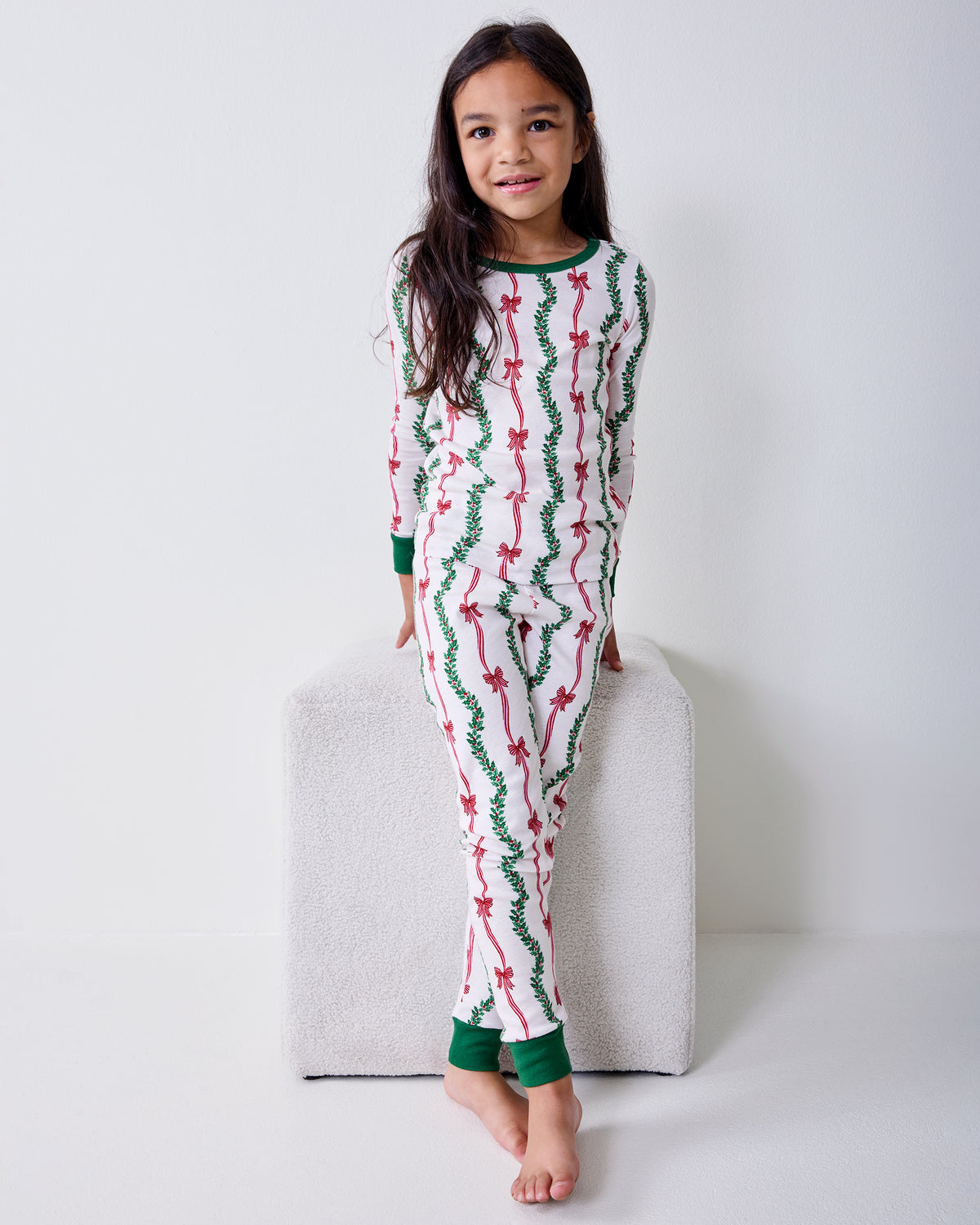 Front view of a child wearing the Ribbons & Bows Vanilla Cream kids long pajama set with green neckline, cuffs, and ankle bands.