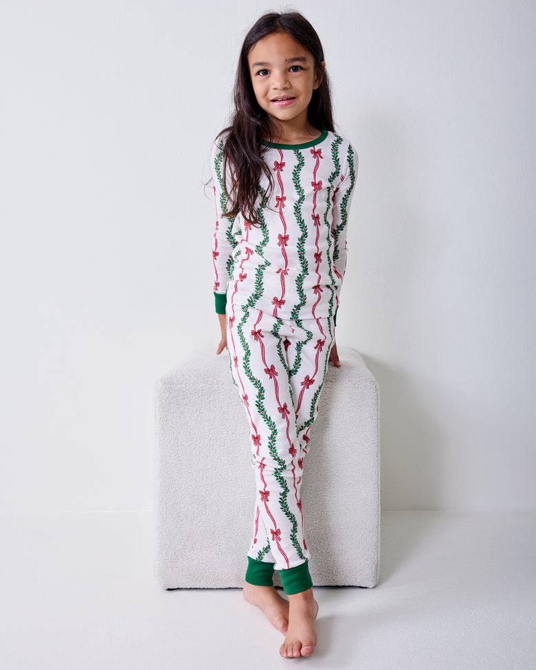 Front view of a child wearing the Ribbons & Bows Vanilla Cream kids long pajama set with green neckline, cuffs, and ankle bands.