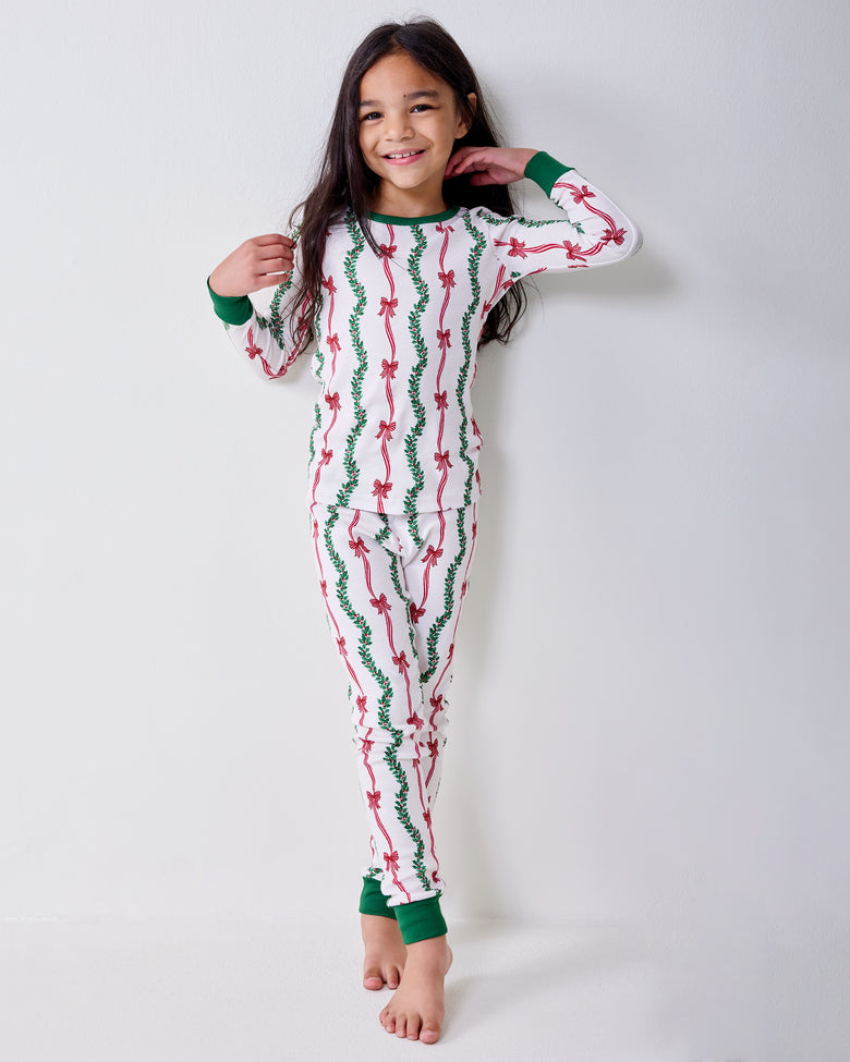 Front view of a child wearing the Ribbons & Bows long pajama set with green cuffs and pink bow and garland print.