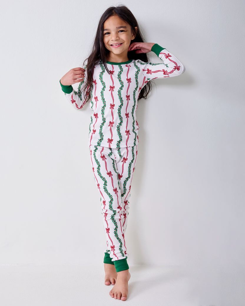 Front view of a child wearing the Ribbons & Bows long pajama set with green cuffs and pink bow and garland print.