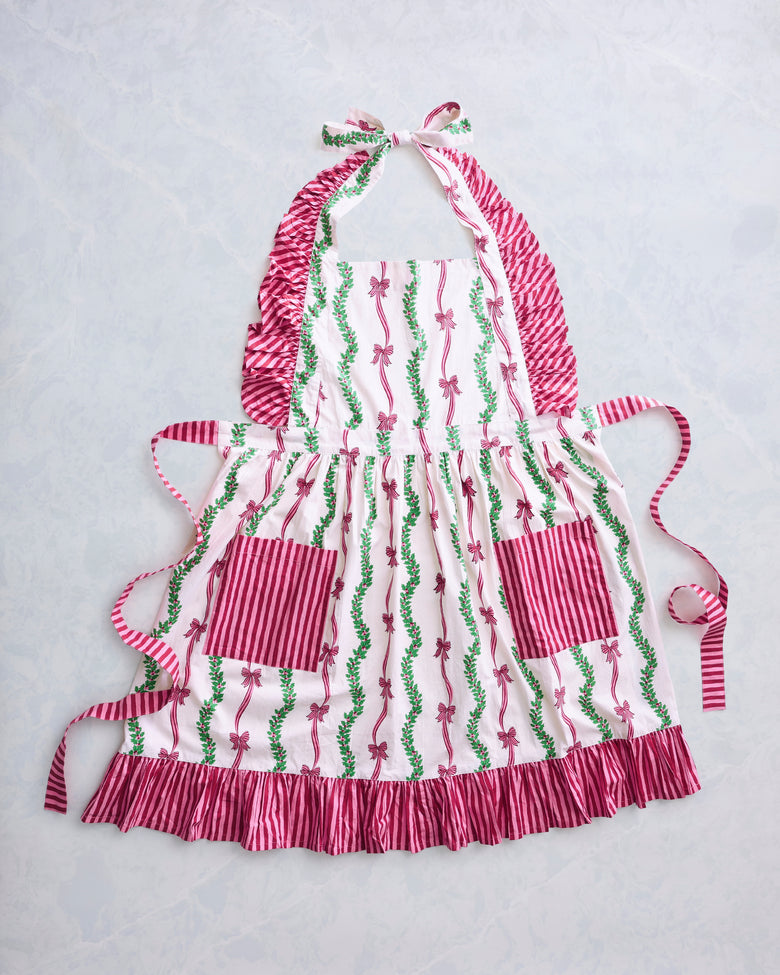 Ribbons & Bows ruffle apron laid flat, with striped ties, two front pockets, and a bow-and-greenery print.