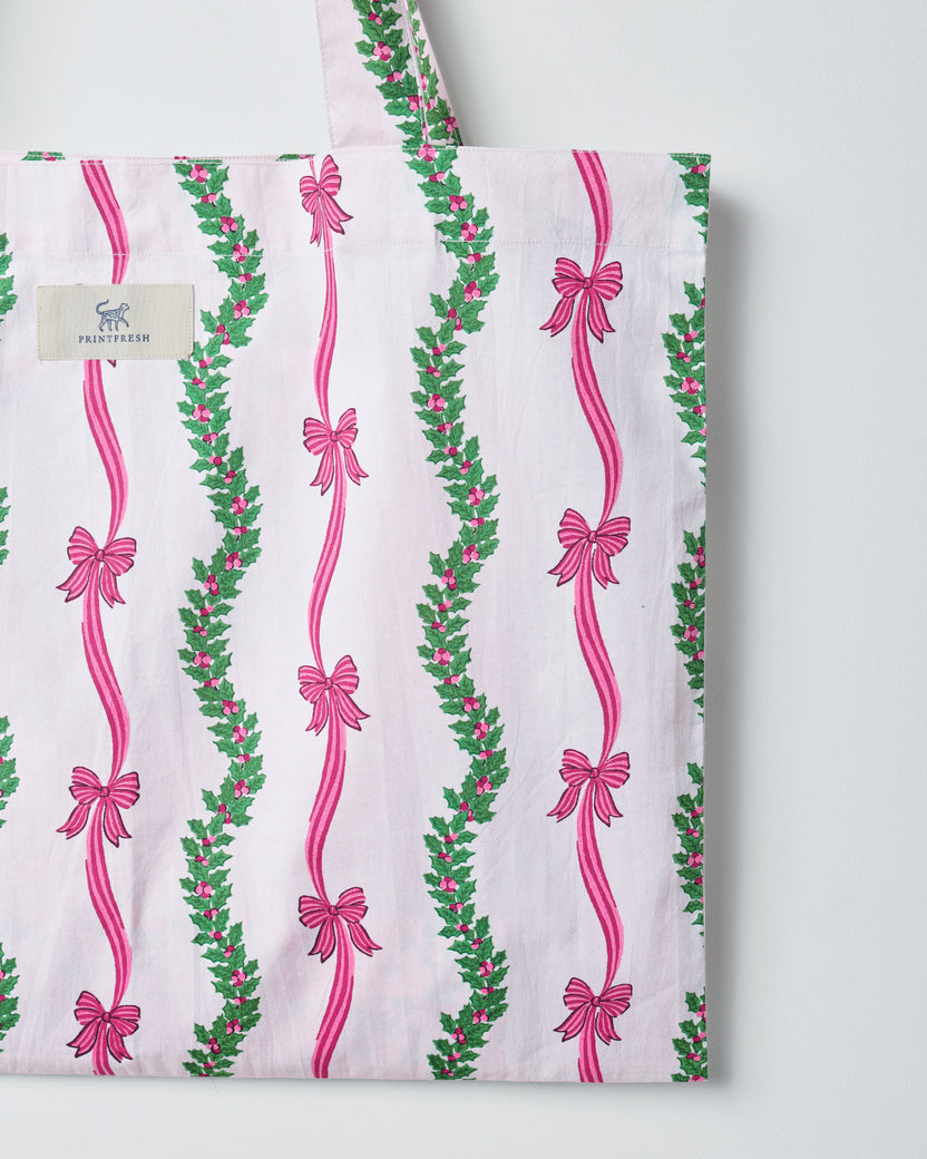 Vanilla cream tote bag with vertical pink ribbon bows and green floral garland stripes, shown from the front.