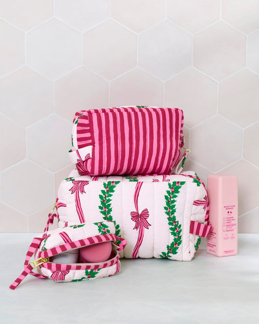 Three quilted pouches in the Ribbons & Bows print, stacked beside an open pouch and a pink bottle.