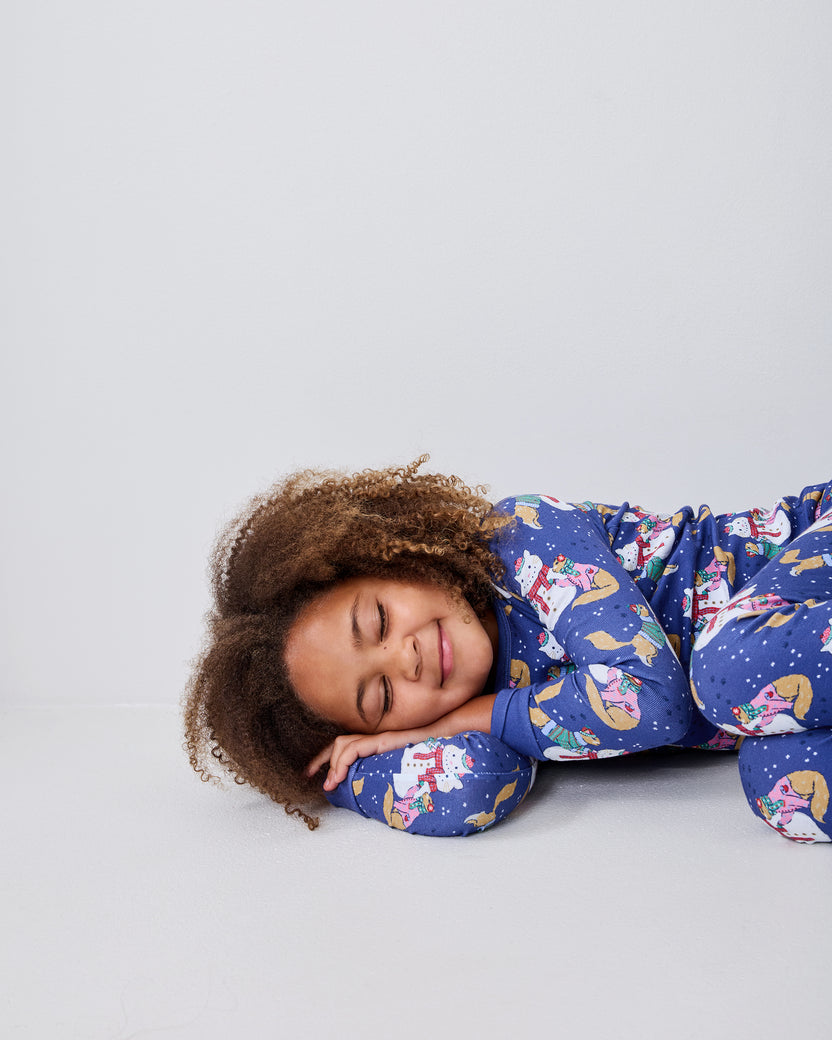 Child lying on the floor wearing blue long-sleeve pajamas with a snowman, cat, and winter print.