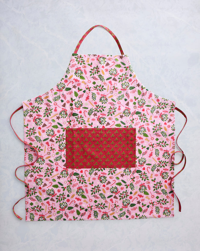 Candy pink apron with a colorful holiday candy and foliage print, front pocket, neck loop, and side ties.