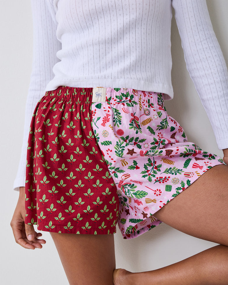 Close-up of two-tone boxer shorts showing the elastic waistband and pink candy-patterned leg beside the red holly-patterned leg.
