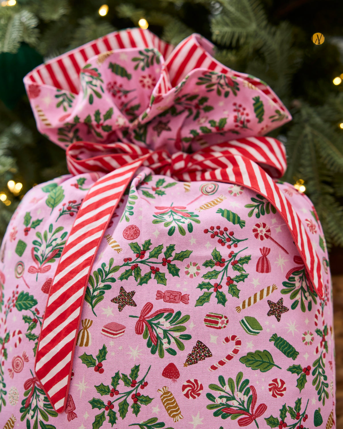 Close-up of a pink holiday-patterned gift sack tied with a red-and-white striped bow.
