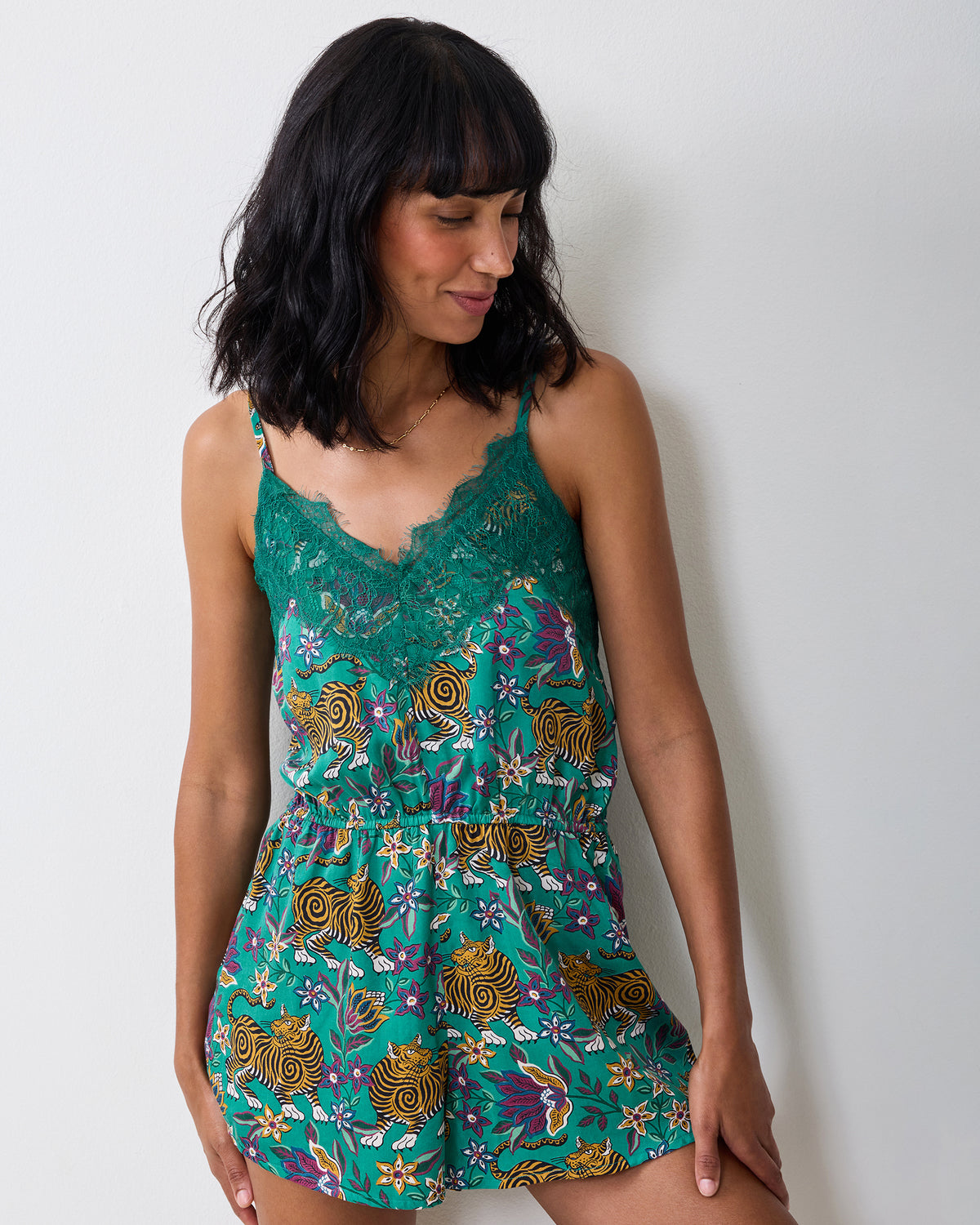 Person standing in the Royal Teal Tibetan Tigress Madeline romper, showing its lace-trimmed neckline, shoulder straps, and patterned shorts.