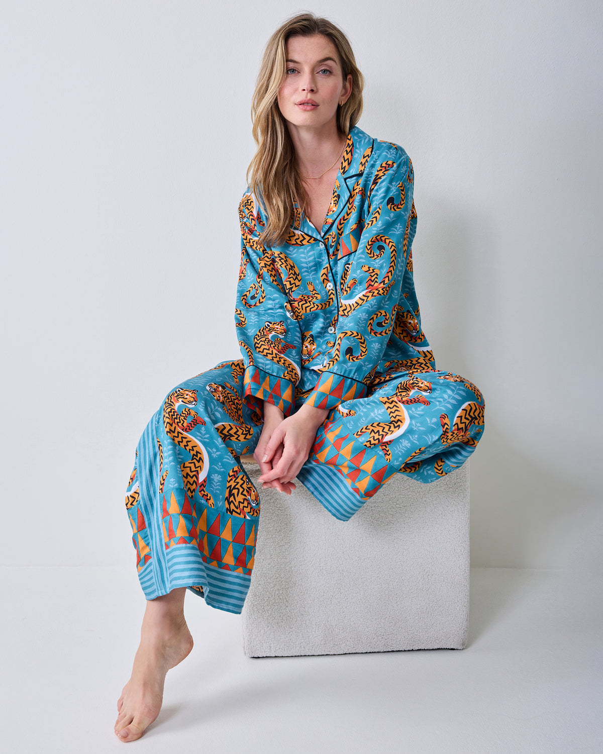 Model seated wearing the Persian Turquoise Twisted Tiger pajama set with a collared button-front top, wide-leg pants, and geometric cuffs and hems.