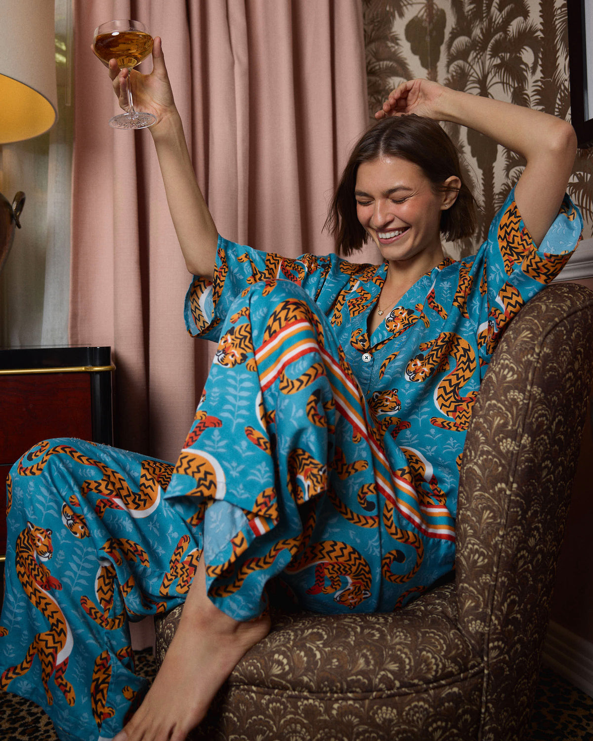 Model reclining in a turquoise tiger-print pajama set while holding a stemmed glass.