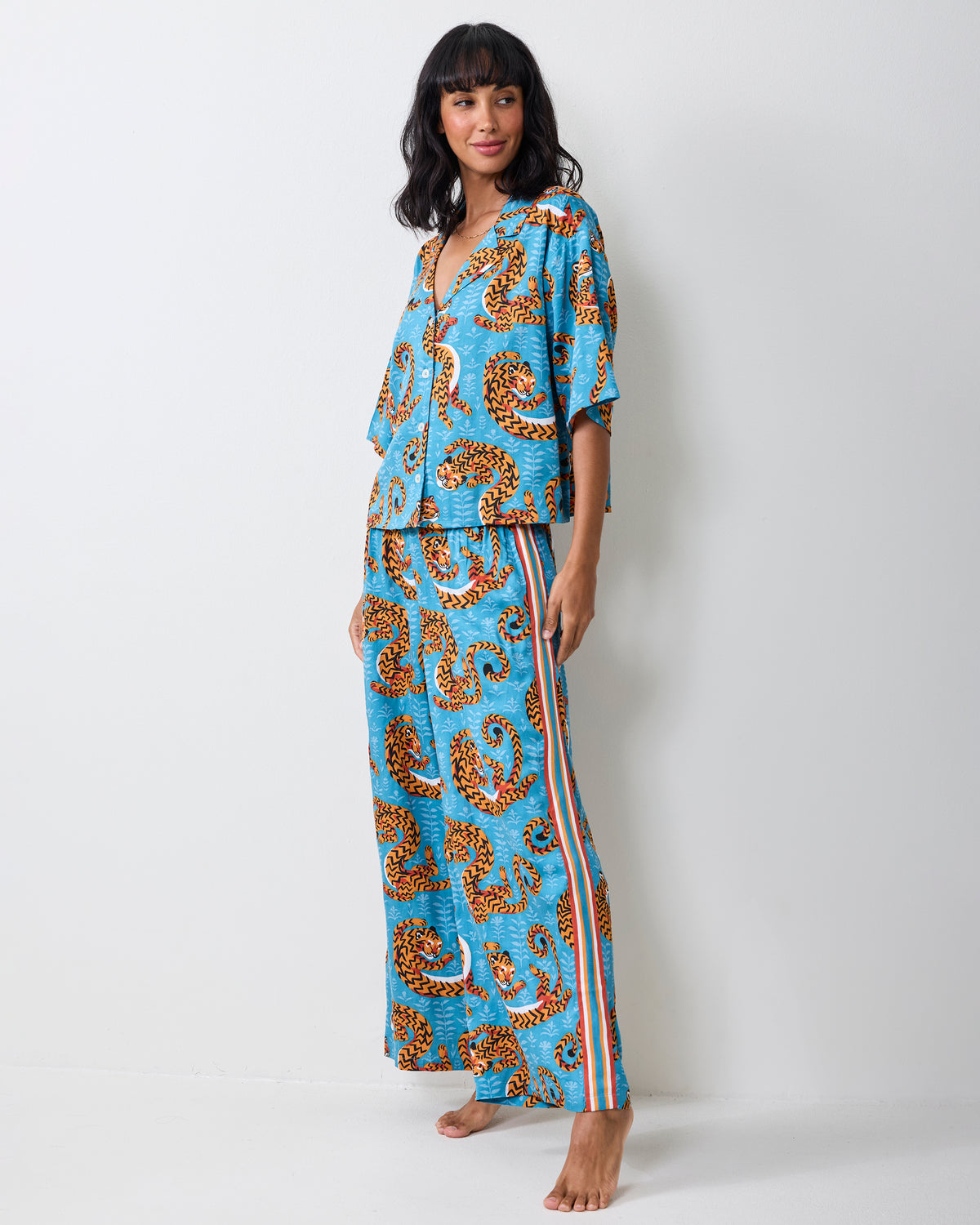 Front three-quarter view of a person wearing the turquoise Twisted Tiger pajama set with wide-leg pants and striped side trim.
