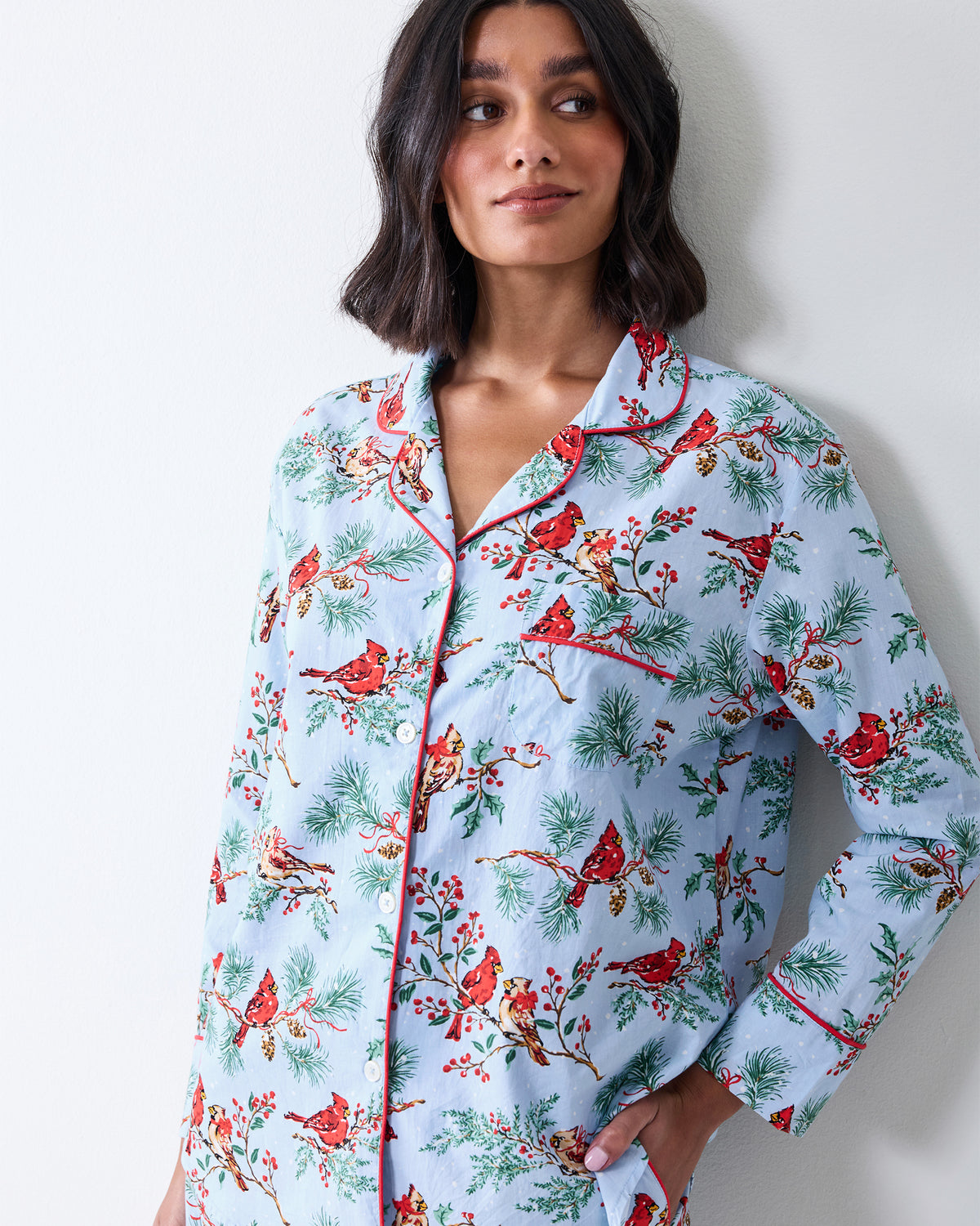 Close-up front view of the frosted blue Winter Cardinals pajama shirt showing the collar, buttons, red piping, chest pocket, and printed birds and greenery.