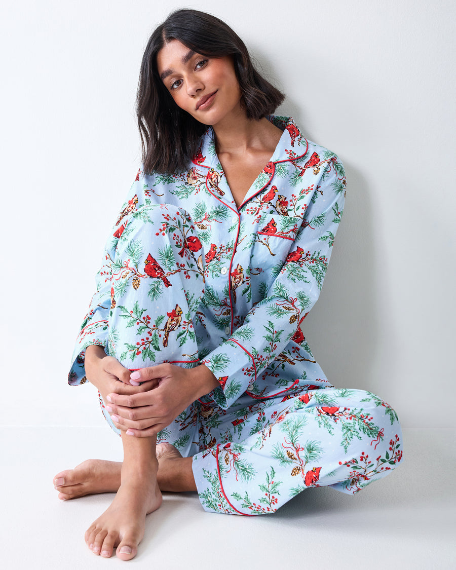 Seated view of the frosted blue Winter Cardinals long pajama set with a long-sleeve button-front shirt and matching long pants.