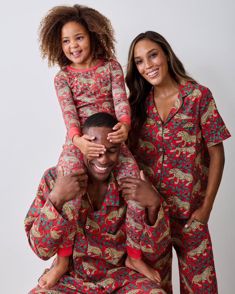 Child wearing a ruby Winter Holly Bagheera long pajama set sits on an adult's shoulders; both wear matching leopard-and-holly prints.