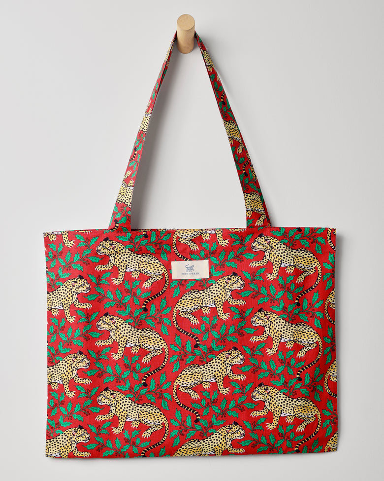 Red Winter Holly Bagheera tote hanging from a wooden peg, showing spotted leopards and green holly leaves across the bag.