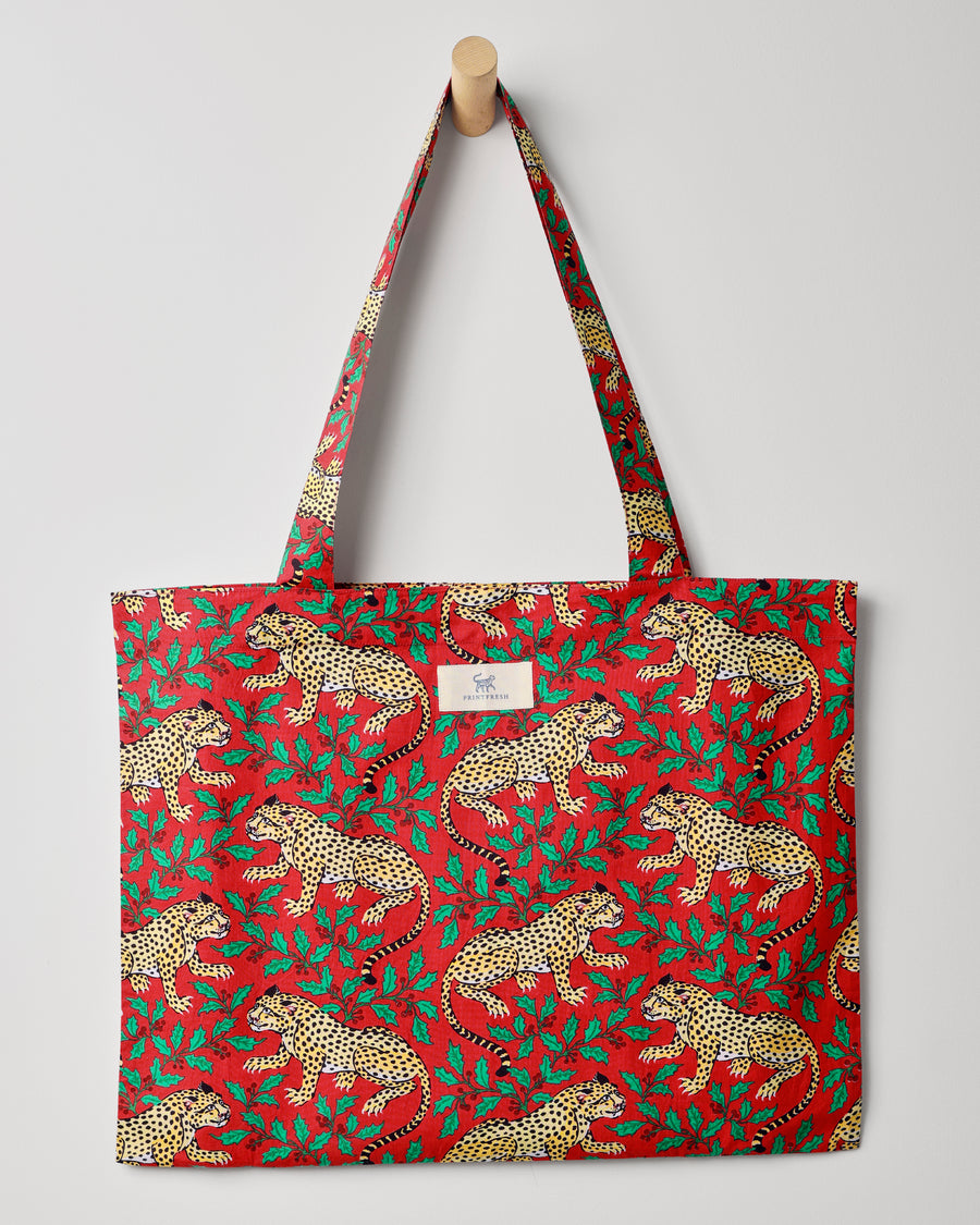 Red Winter Holly Bagheera tote hanging from a wooden peg, showing spotted leopards and green holly leaves across the bag.