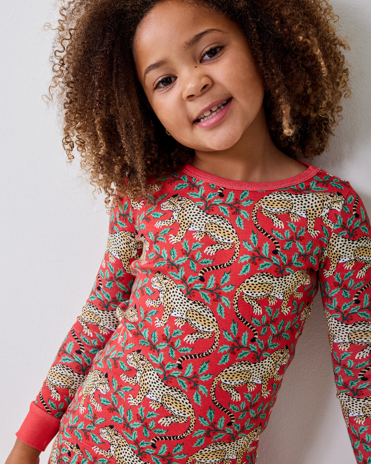 Child wearing a red long-sleeved top patterned with leopards and leafy shapes.