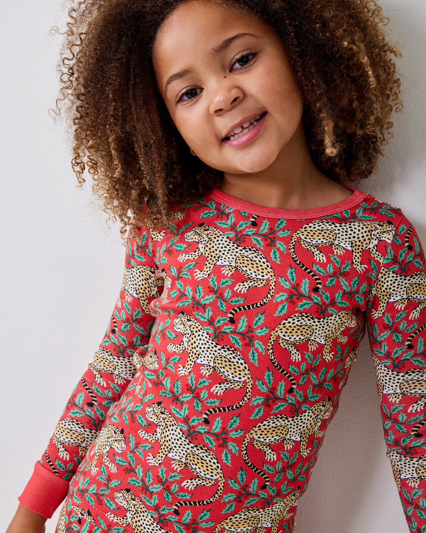 Child wearing a red long-sleeved top patterned with leopards and leafy shapes.