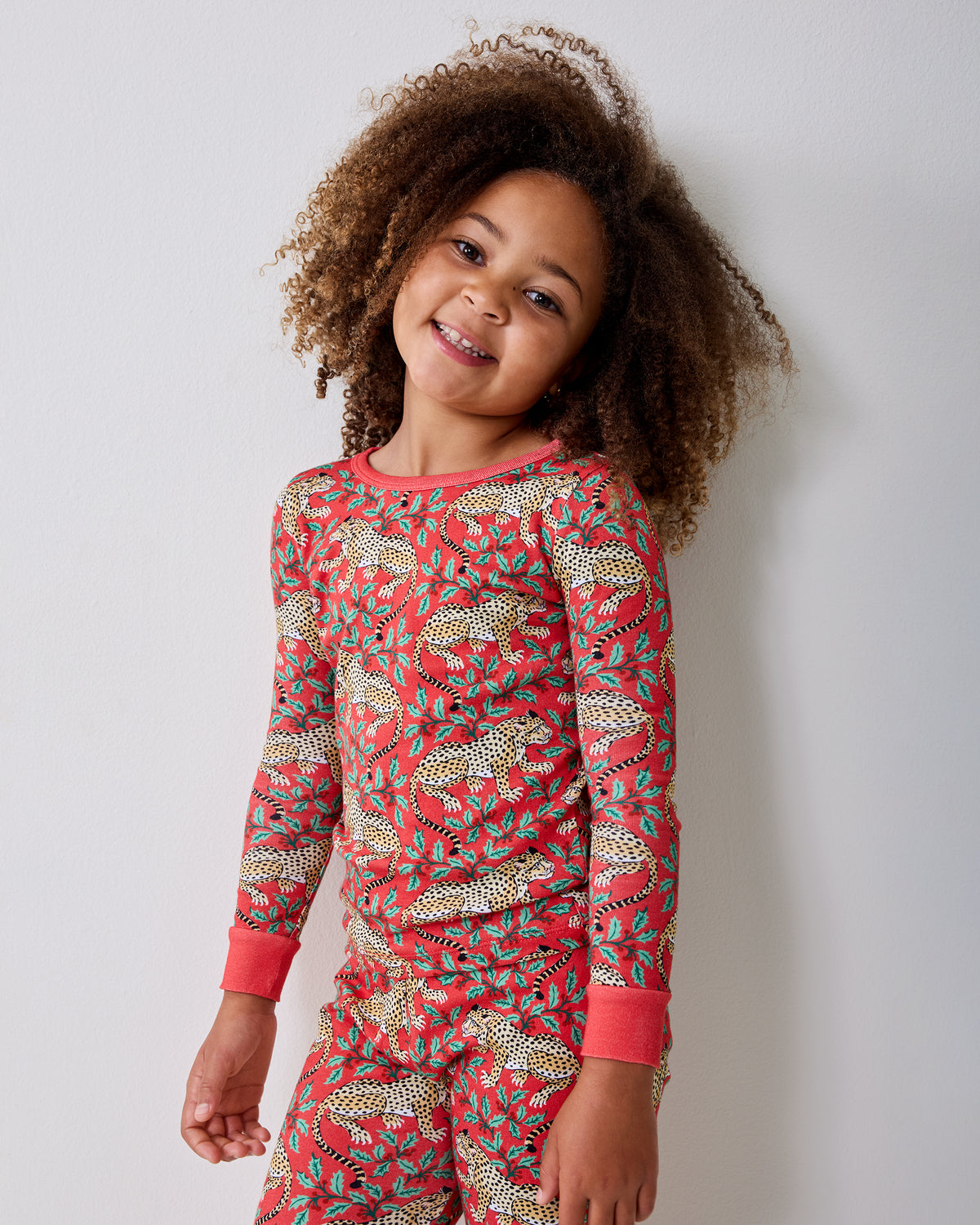 Child modeling a red long-sleeve pajama set with spotted leopards and holly leaves.