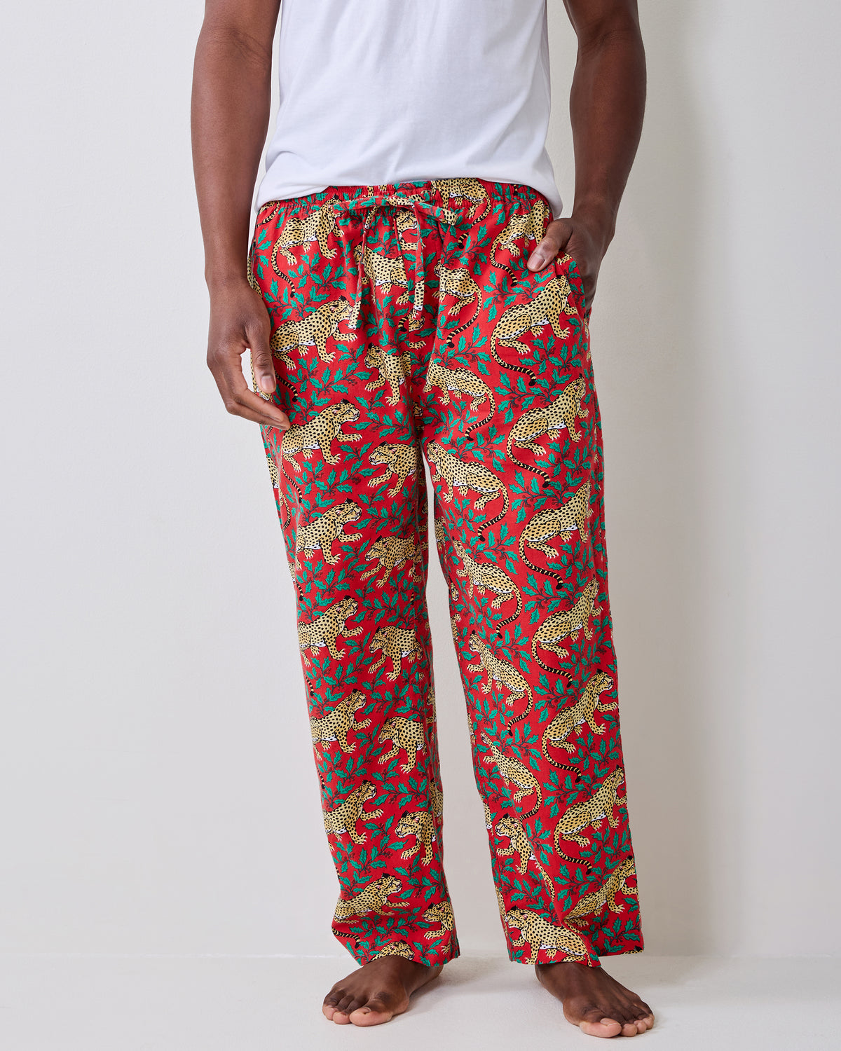 Close front view of red pajama pants with a repeating leopard-and-leaf print and drawstring waist.