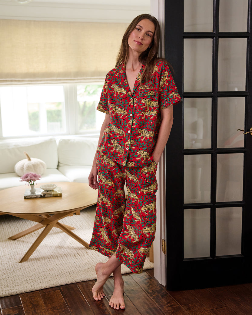 Person standing indoors wearing the red Winter Holly Bagheera pajama set with a button-down top and cropped pants.