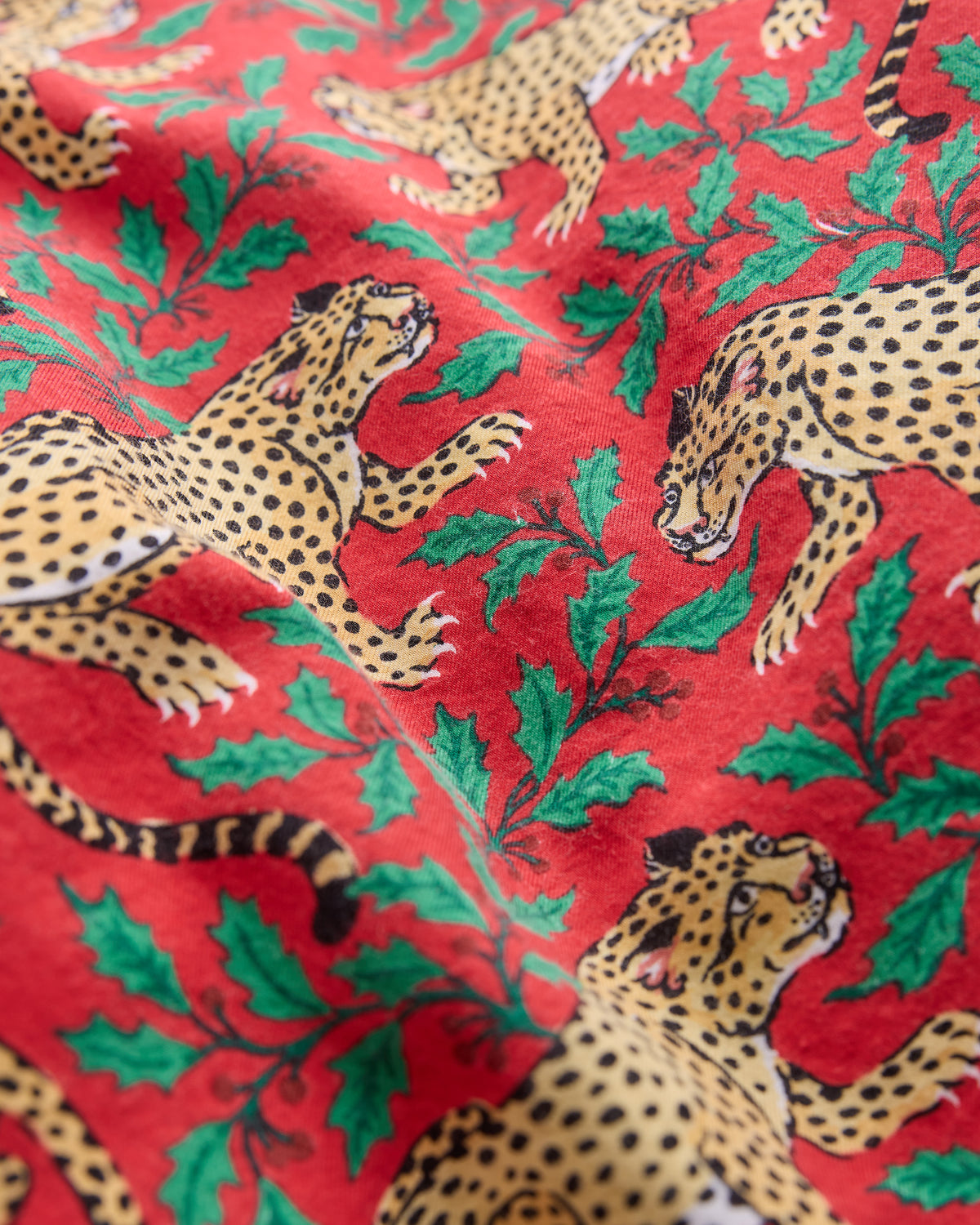 Close-up of red pajama fabric printed with spotted leopards and green holly leaves.