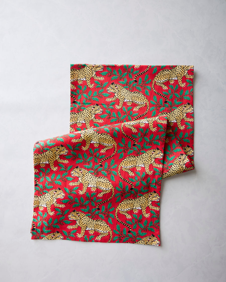 Red table runner with a repeating leopard-and-holly pattern, folded over itself.