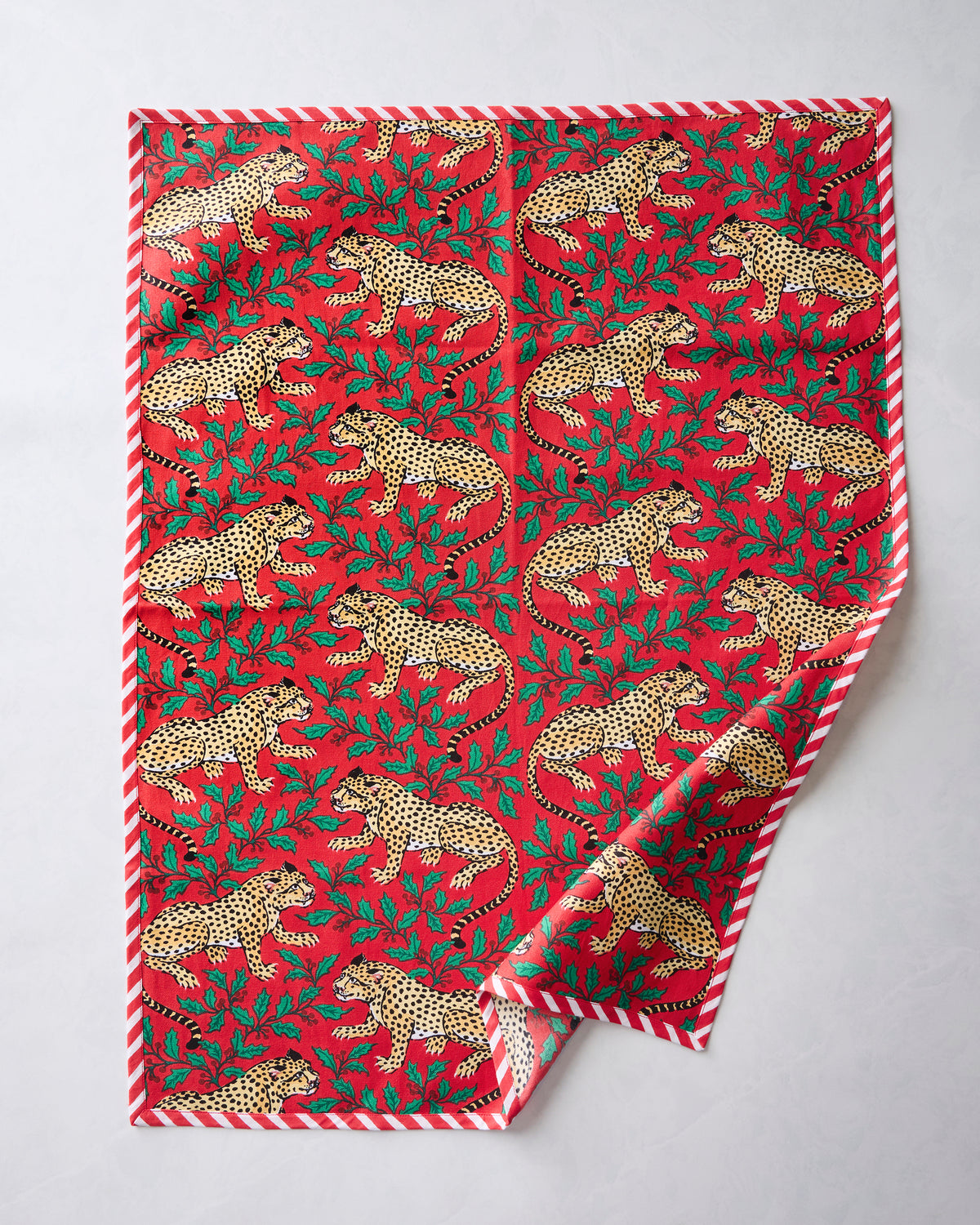 Front of a Winter Holly Bagheera tea towel with a red leopard-and-holly print and red-and-white striped border.
