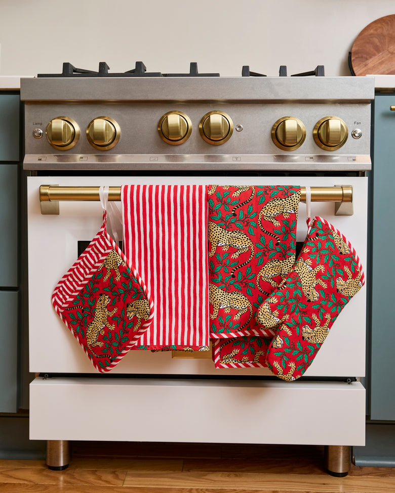 Two red patterned tea towels and a matching oven mitt hanging from a range handle.