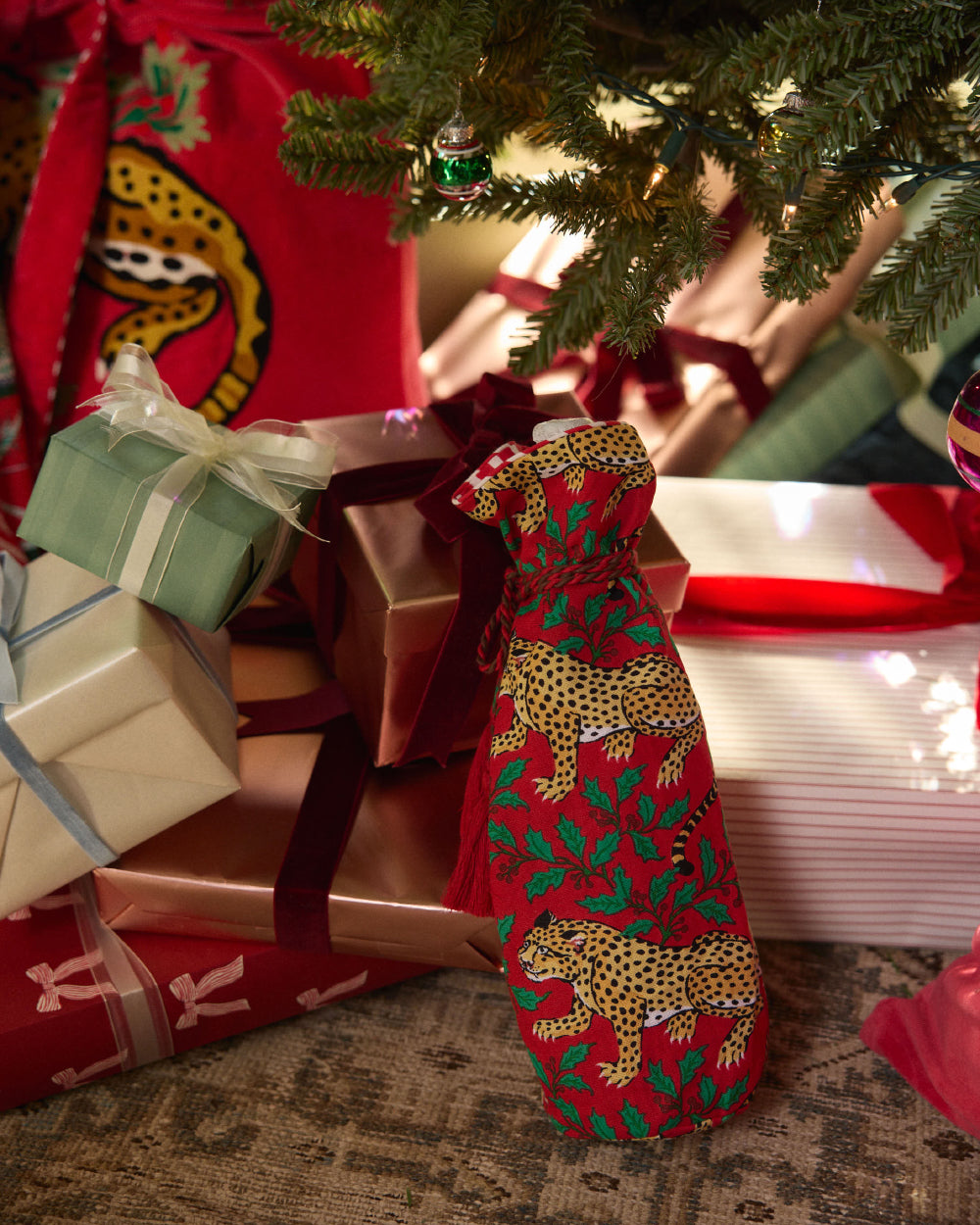 Winter Holly Bagheera ruby wine bag displayed beside wrapped gifts under a Christmas tree.