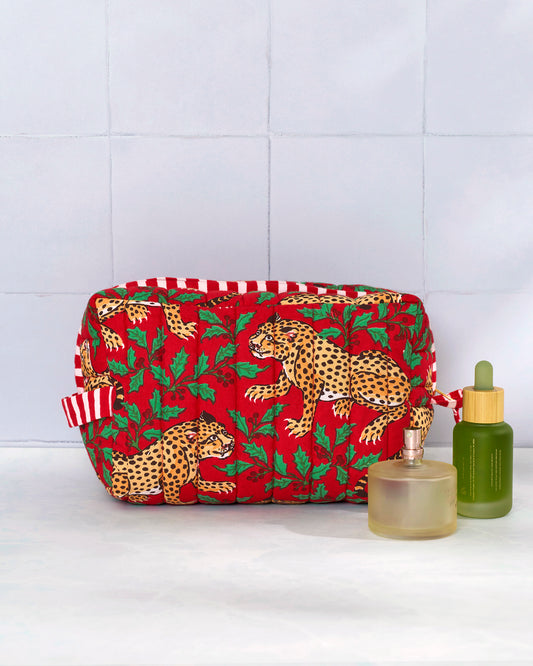 Winter Holly Bagheera quilted pouch displayed with a small bottle and perfume bottle beside it.
