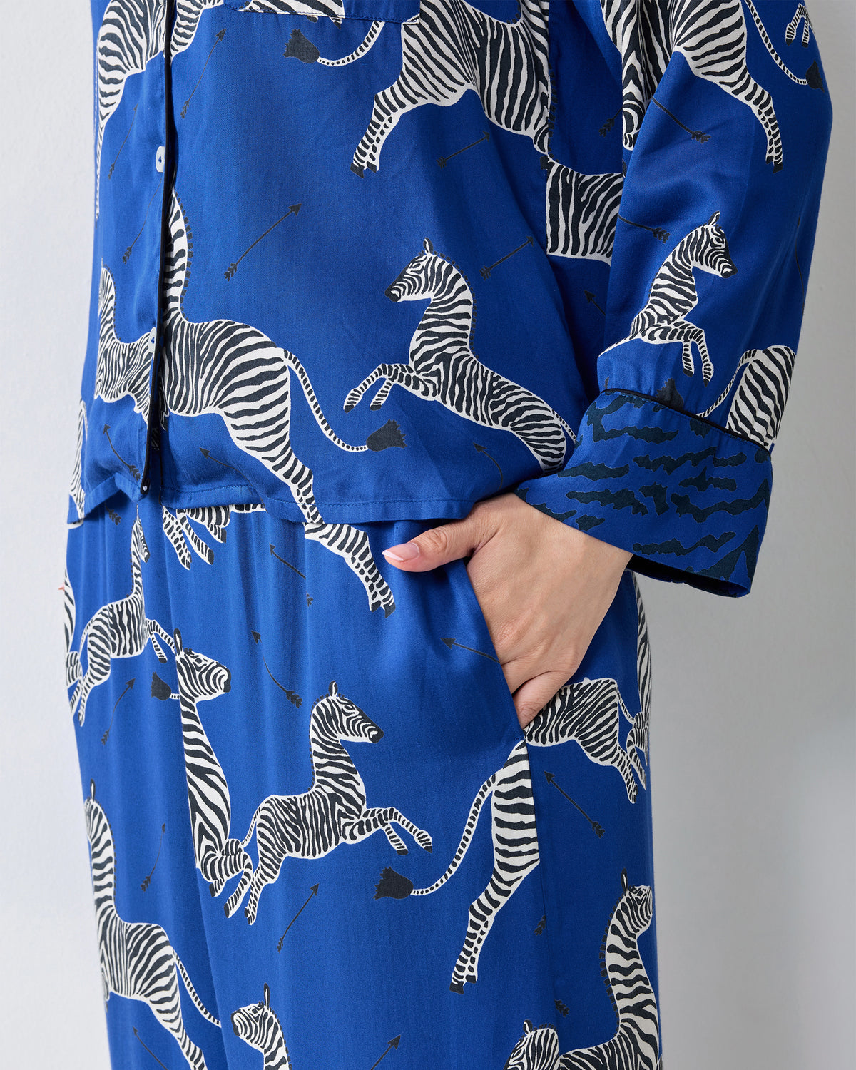 Close-up of a hand in the pocket of blue zebra-print pajama pants beneath a matching button-front top.