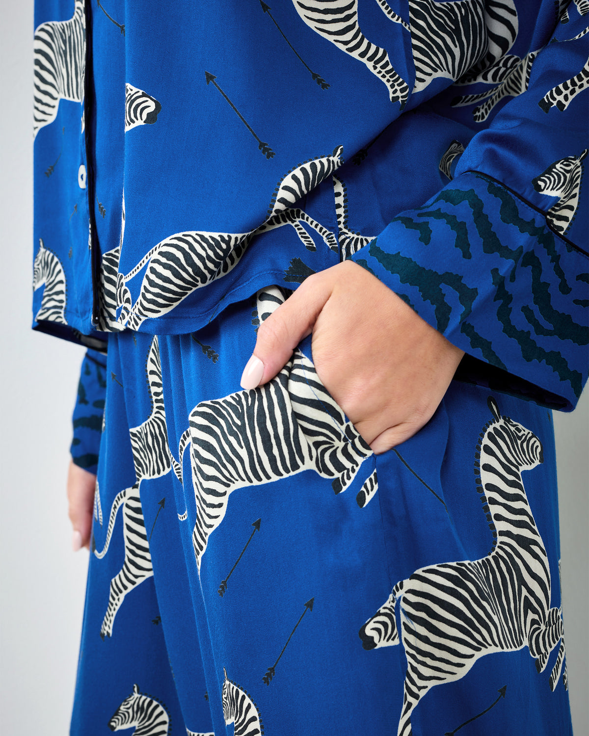 Close-up of a hand in the pocket of blue zebra-print pajama pants, with the matching top and cuff visible.
