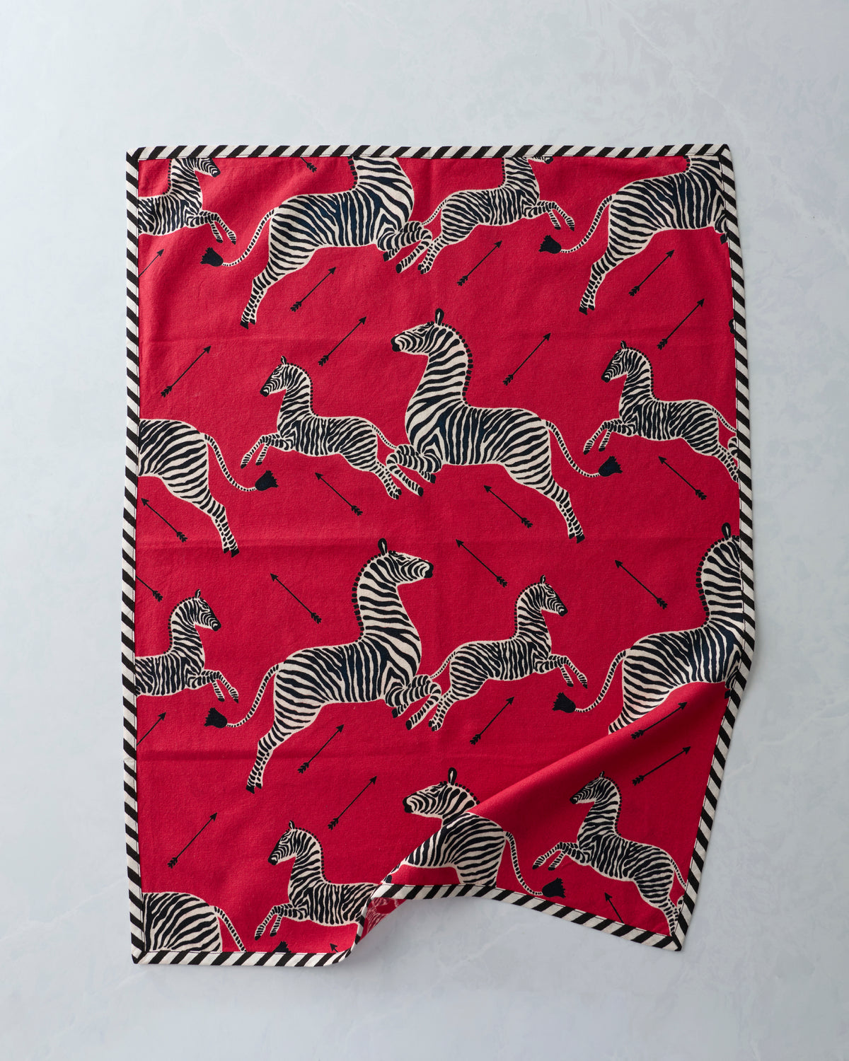 Red tea towel spread flat with repeated zebra print and black-and-white striped edging