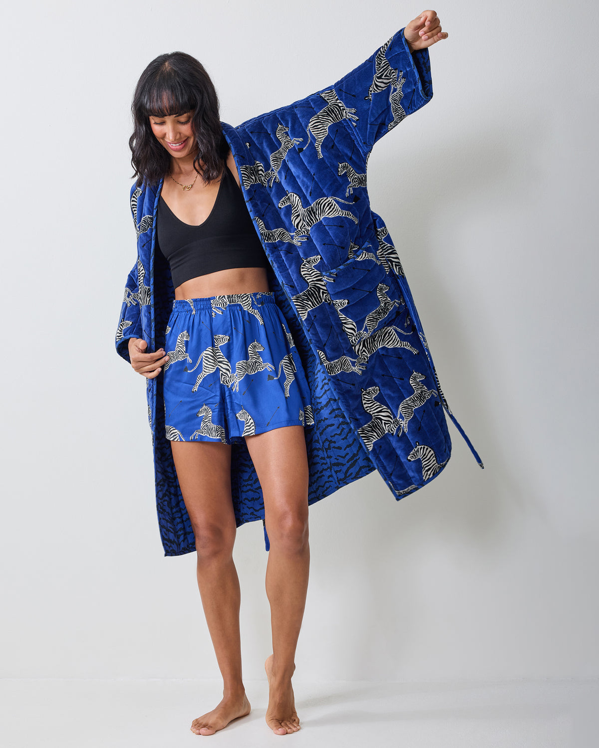 Person wearing a long blue zebra-print quilted robe over a black top, shown full length with one arm raised