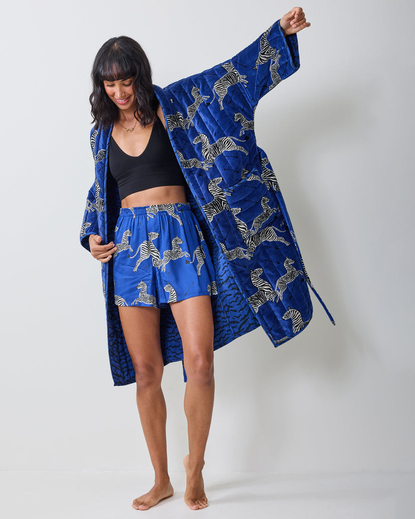 Person wearing a long blue zebra-print quilted robe over a black top, shown full length with one arm raised