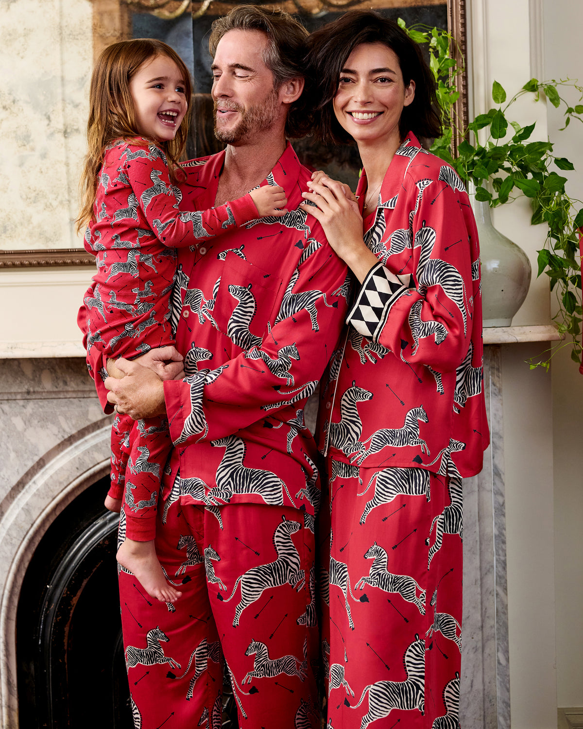 Adults and a child wearing matching Masai red zebra-print pajama sets indoors.