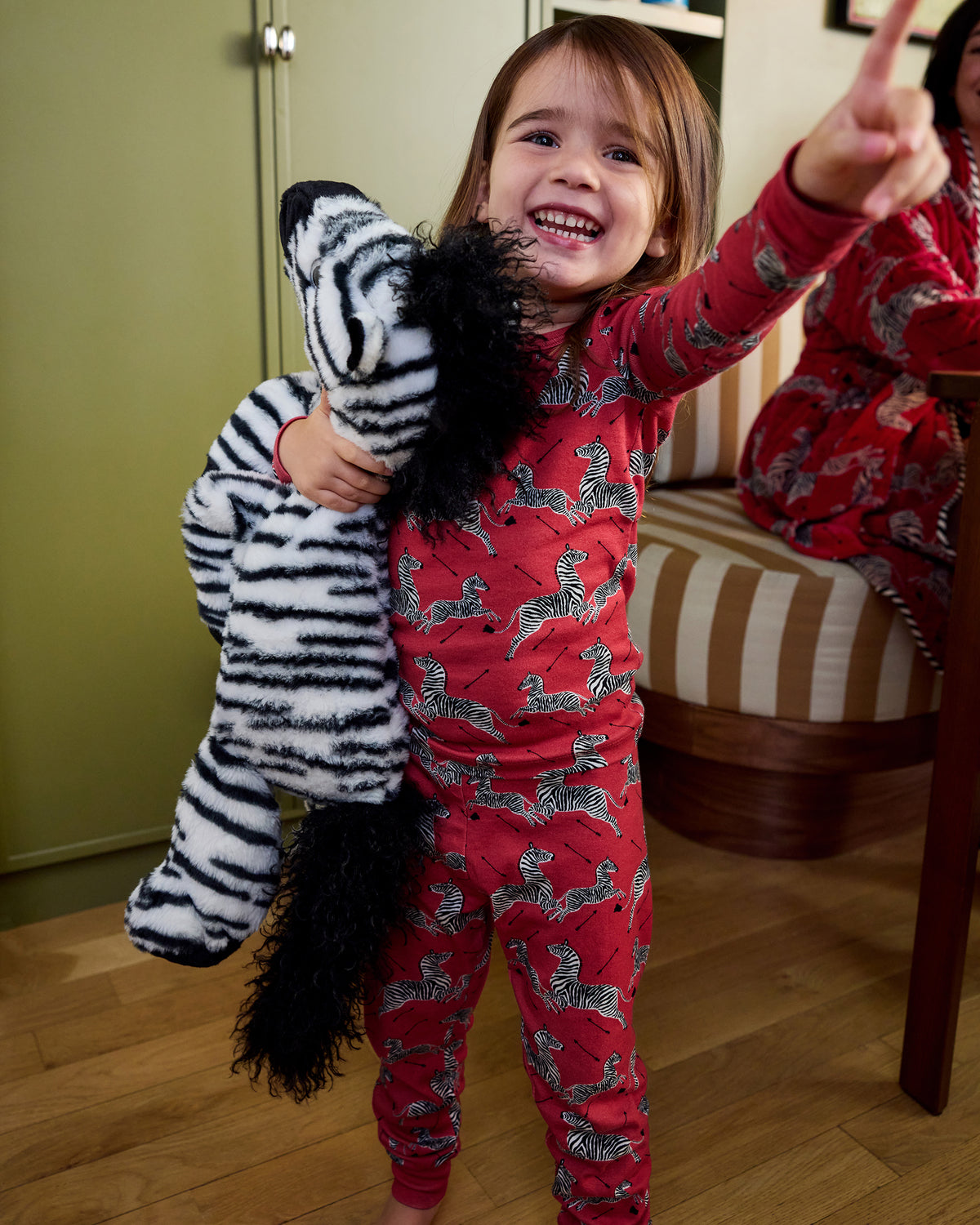 Child wearing a red zebra-print pajama set while holding a black-and-white zebra plush toy.