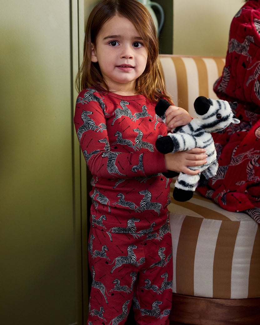 Child wearing a red long-sleeve zebra-print pajama set and holding a zebra plush toy.