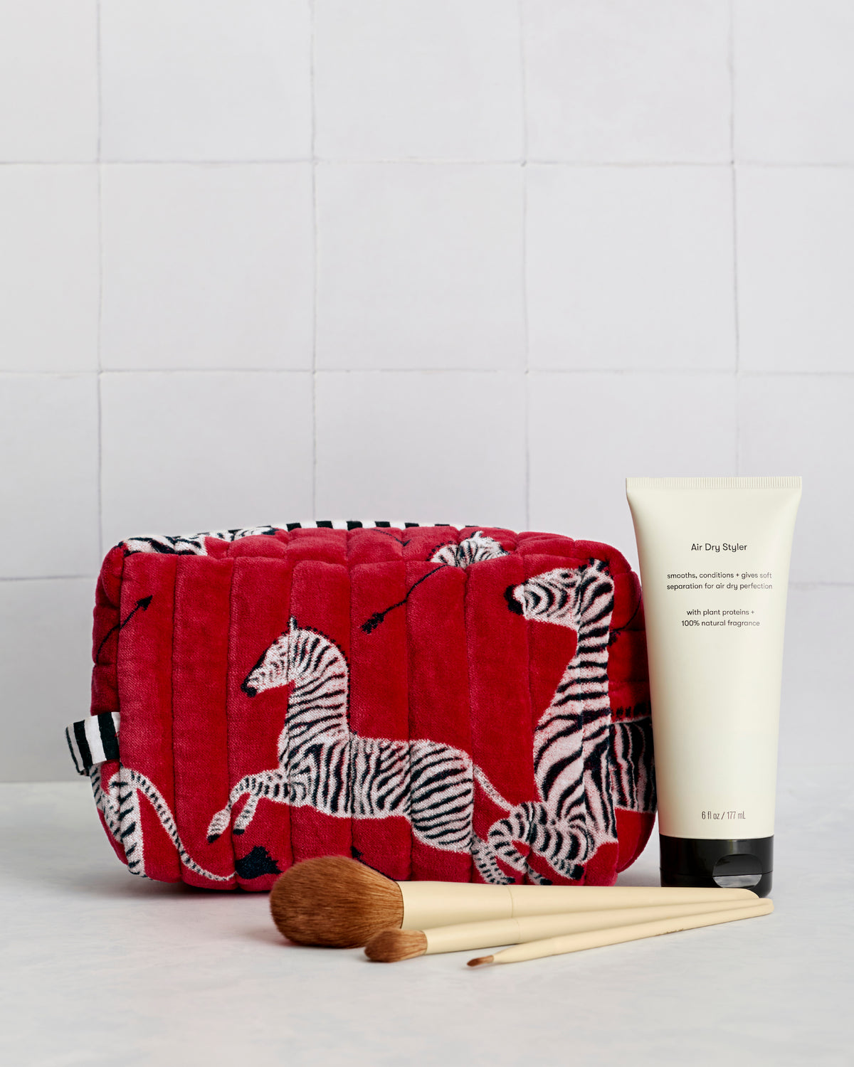 Red quilted zebra-print pouch displayed beside a cream tube and makeup brushes.
