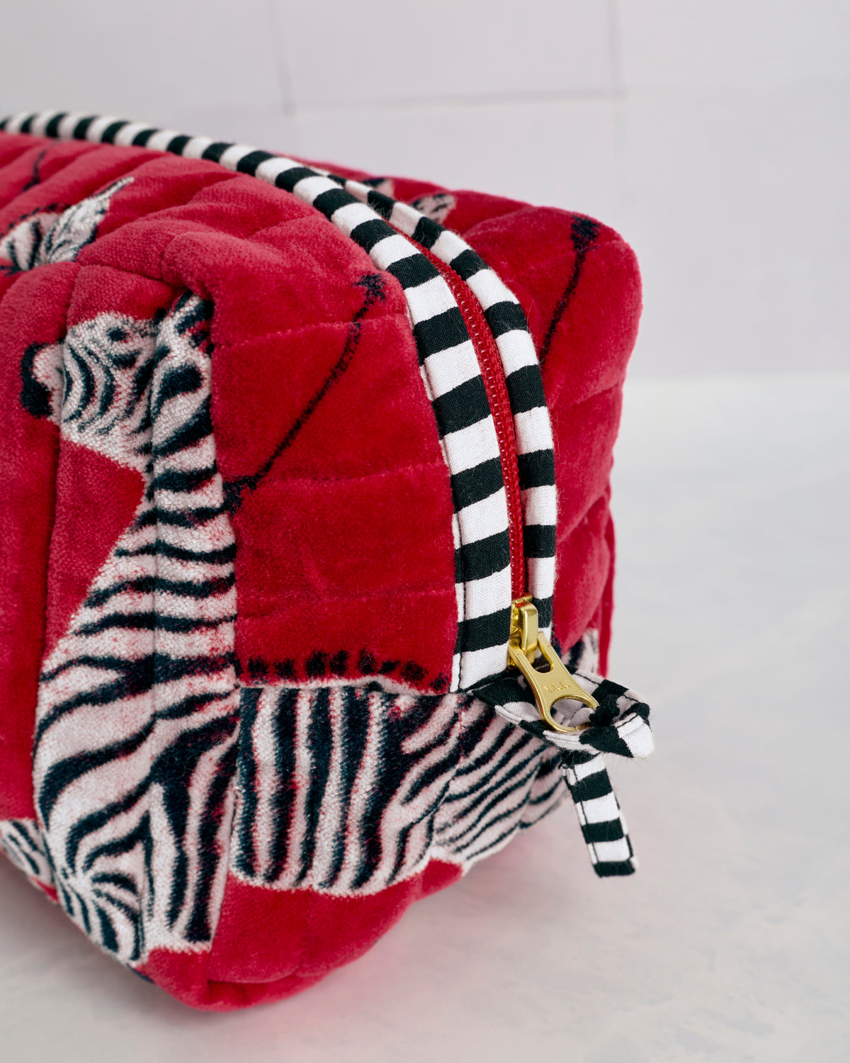 Close-up of the red quilted zebra-print pouch showing black-and-white striped trim and a gold zipper pull.