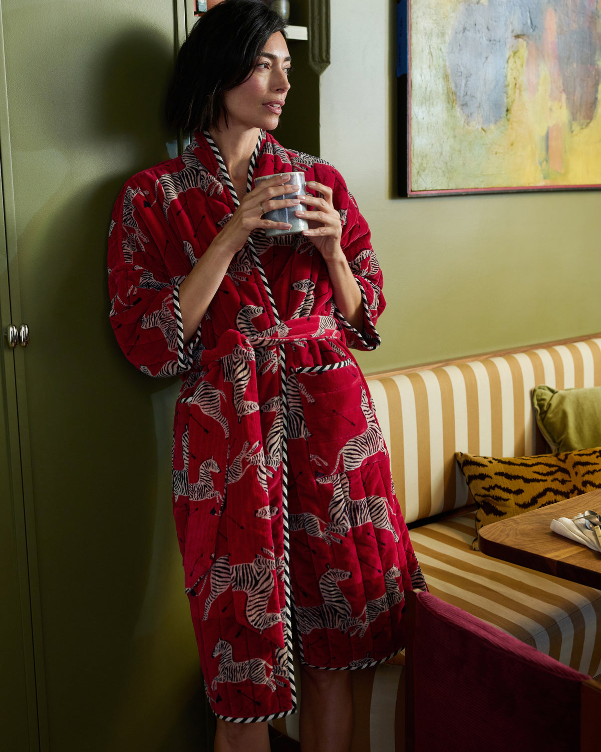 Person wearing a red zebra-print quilted robe with a belt and pockets while holding a mug.