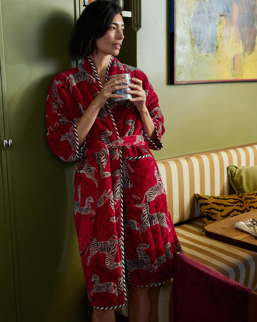 Person wearing a red zebra-print quilted robe with a belt and pockets while holding a mug.